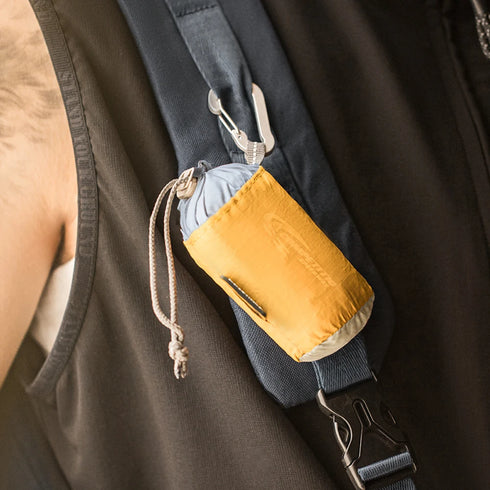 Yellow pouch attached to a backpack strap with a person wearing a brown sleeve in the background.